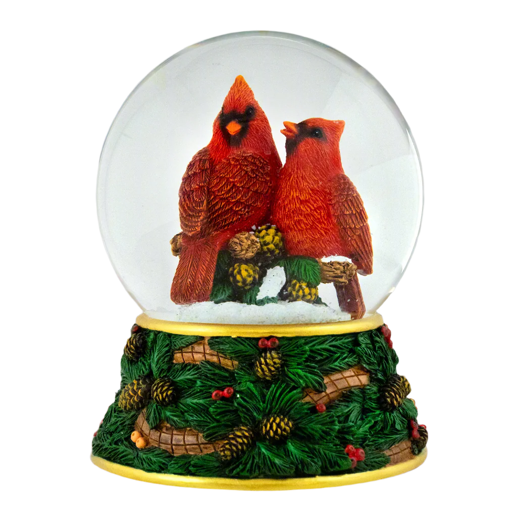 Snow globe with two cardinals on a branch inside, surrounded by pinecones and leaves